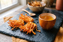Champignons cordyceps militaris orange vif sur ardoise sombre avec tasse de boisson dorée